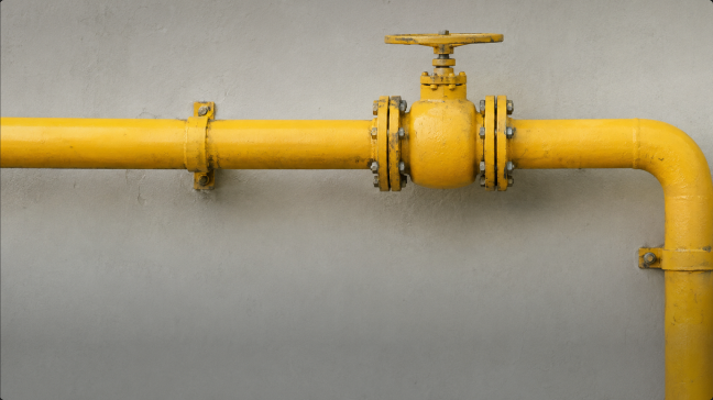 Yellow gas pipeline with a hand valve on a concrete wall
