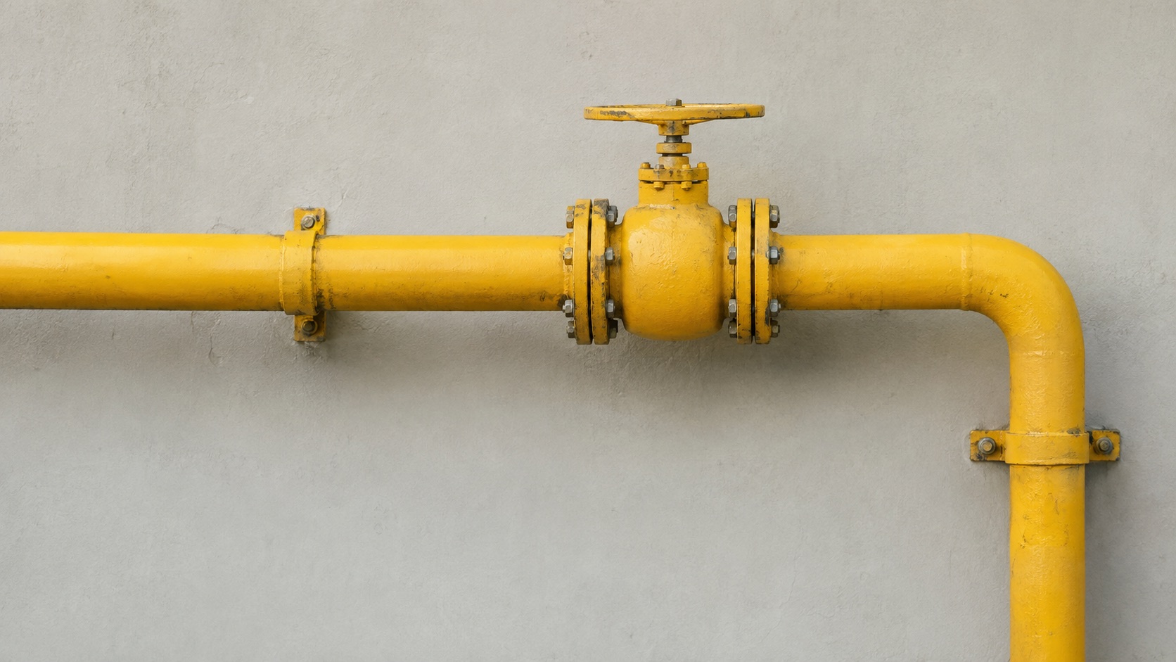 Yellow gas pipeline with a hand valve on a concrete wall